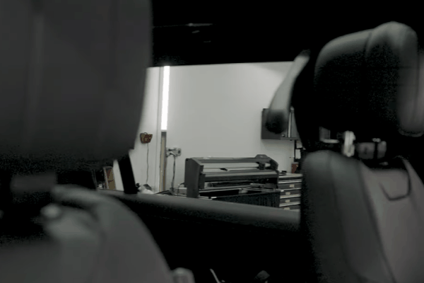 a technician applying window tint film to a car’s side window from the interior, demonstrating precision installation in a professional auto shop setting.