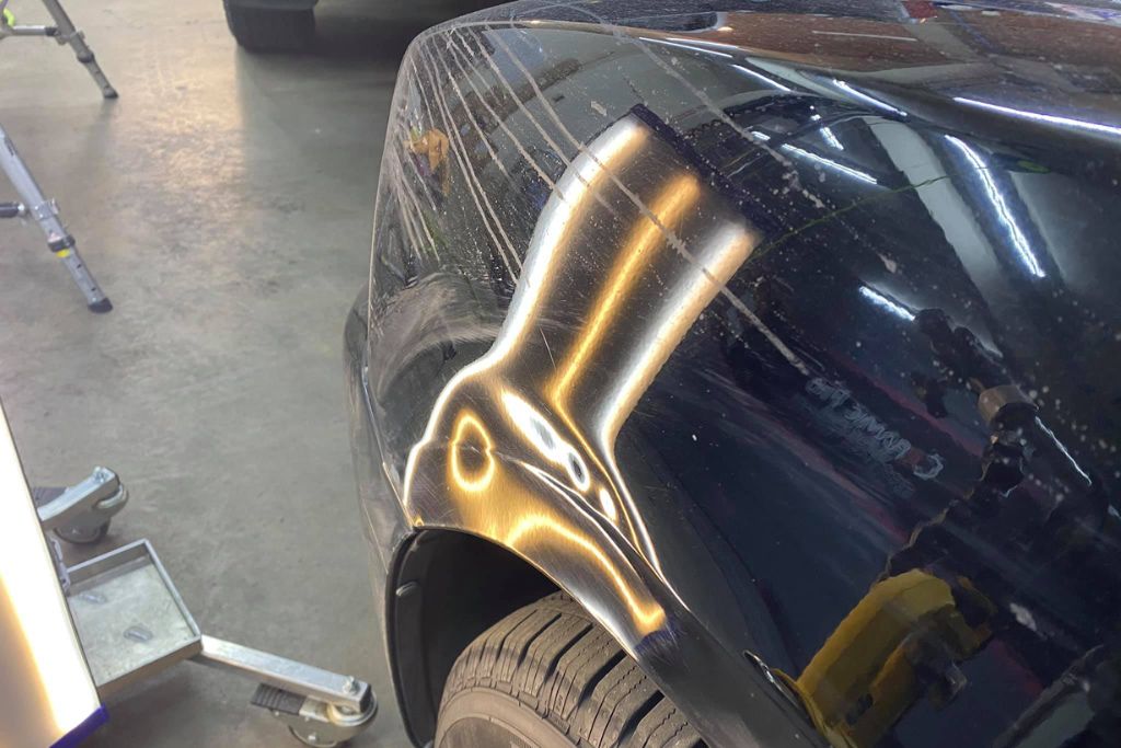 Close-up of a black vehicle's fender showing swirl marks, scratches, and surface imperfections under bright shop lighting, illustrating one of the key disadvantages of ceramic coating—it cannot repair or prevent physical damage like this.