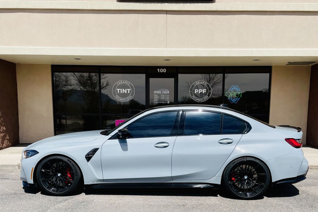 A sleek, professionally detailed gray sedan parked in front of a ceramic coating and PPF service shop, showcasing the long-lasting glossy finish that answers how long does ceramic coating last with proper care.