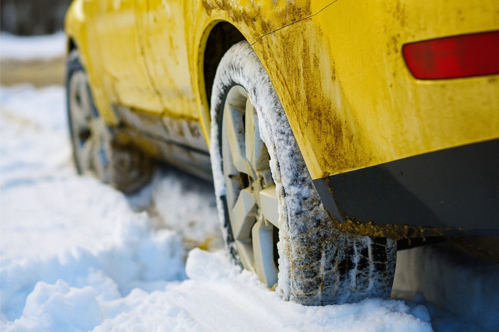 Rear view of a dirty yellow car driving through snow and road salt, illustrating the harsh winter conditions ceramic coating helps protect against in Colorado Springs. This image supports the answer to what is ceramic coating by showing its benefit in resisting salt and grime.