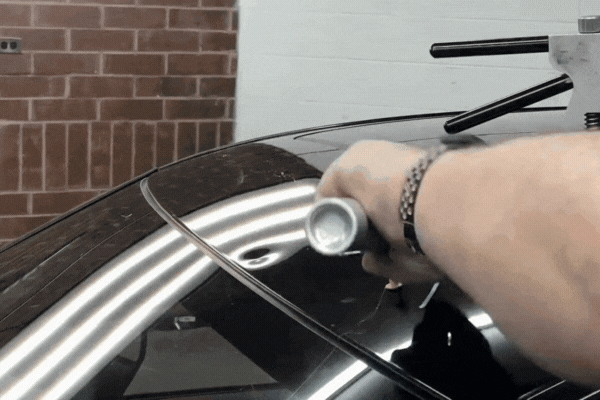 Technician performing paintless dent repair on a black car roof using a specialized light and tool to reshape the metal, showing how PDR works without damaging the paint. A visual guide for Colorado Springs drivers asking What Is Paintless Dent Repair.