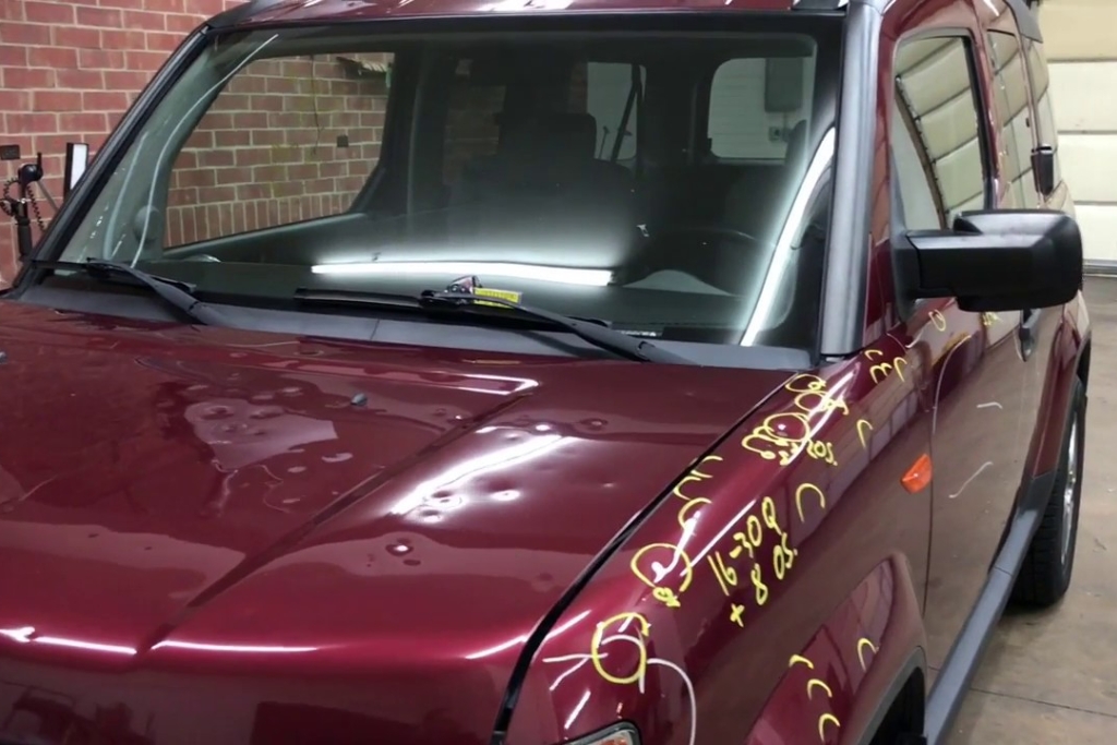 Hail Damage Repair Process shown on a maroon SUV in Colorado Springs with yellow marker circles outlining dents across the hood and fender. The image highlights the thorough damage documentation used to estimate repair time and cost before starting hail restoration work.