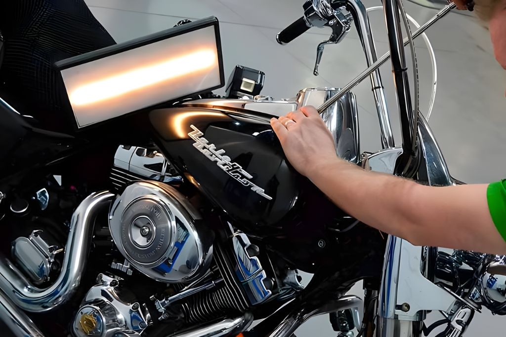 A technician uses a dent removal rod and reflection light to perform paintless dent repair on a black motorcycle tank, demonstrating the hands-on process and time efficiency of motorcycle PDR in Colorado Springs.