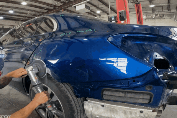 Auto body technician in Colorado Springs uses a power sander on a dented blue SUV rear panel during a Traditional Dent Repair process, showing preparation for filler and repainting.
