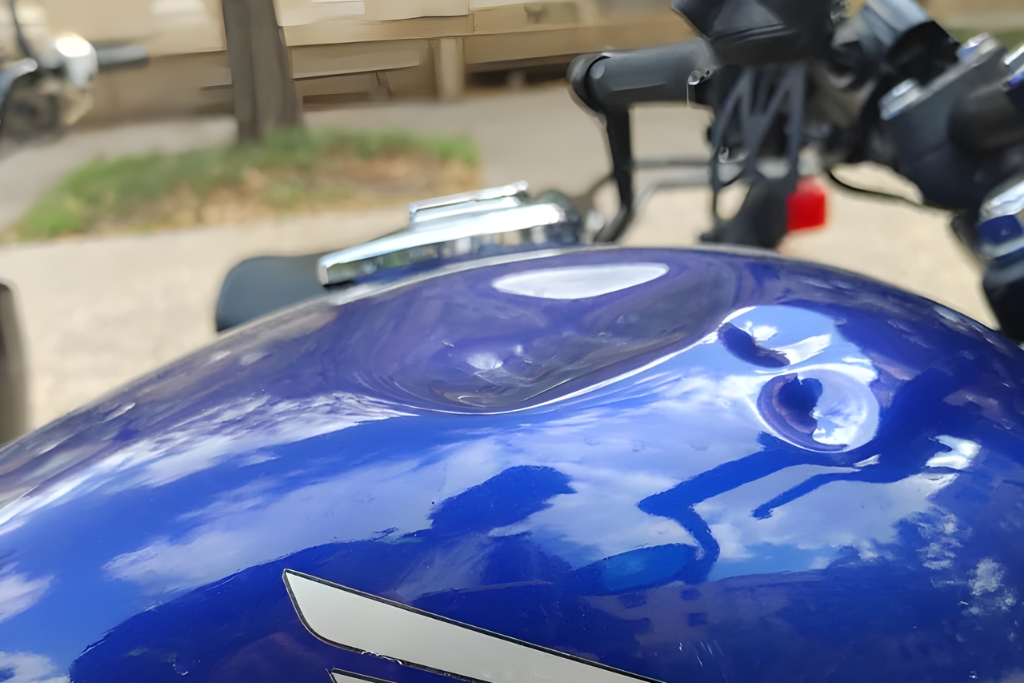 Close-up of a blue motorcycle gas tank with multiple smooth dents and no visible paint damage, illustrating a common example of when PDR is a good fit for motorcycle dents in Colorado Springs.