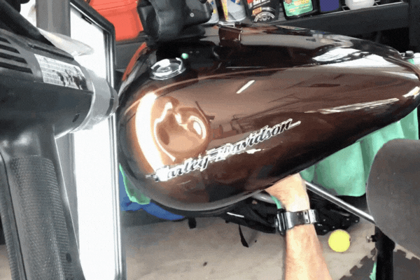 A technician performs paintless dent repair on a brown Harley-Davidson motorcycle gas tank using a reflective board and precision tools, highlighting why motorcycle owners choose paintless dent repair in Colorado Springs.