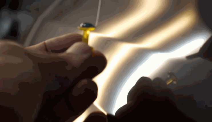 Hands holding a yellow tab for glue pulling, prepping for hail damage repair on a dented car surface.