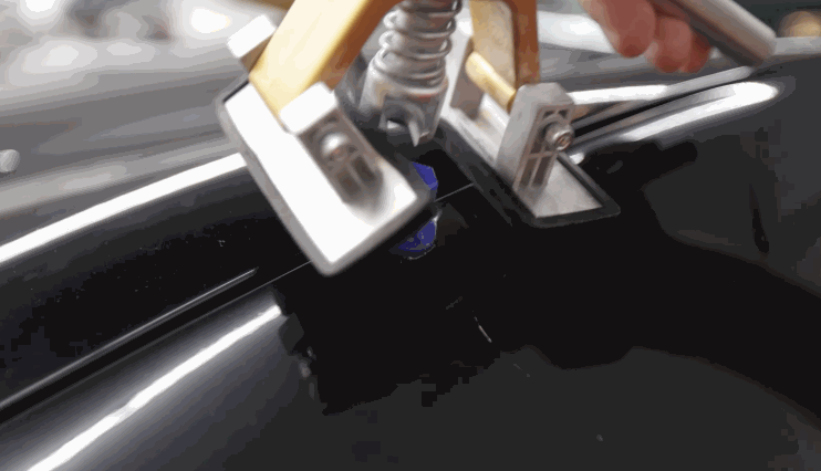 Dent removal tool applying pressure on a blue glue tab during a paintless hail damage repair procedure.