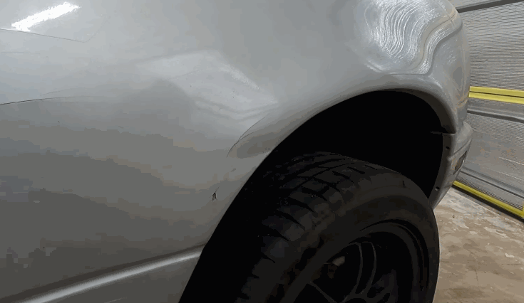 Side view of a silver car’s fender showing a noticeable dent that is being evaluated before starting paintless dent repair.