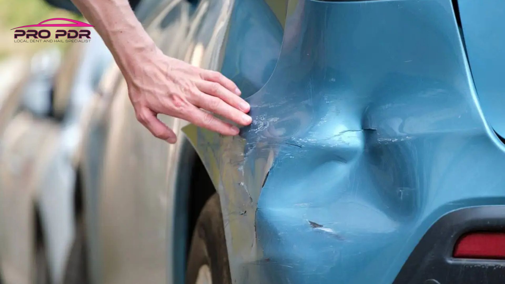 Hand inspecting a large dent and scratch damage on the rear quarter panel of a blue car, highlighting a candidate area for paintless dent repair.