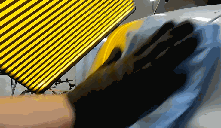 Gloved hand using a microfiber cloth to clean the car surface after a dent is pulled, with a striped reflection board showing a smooth panel.