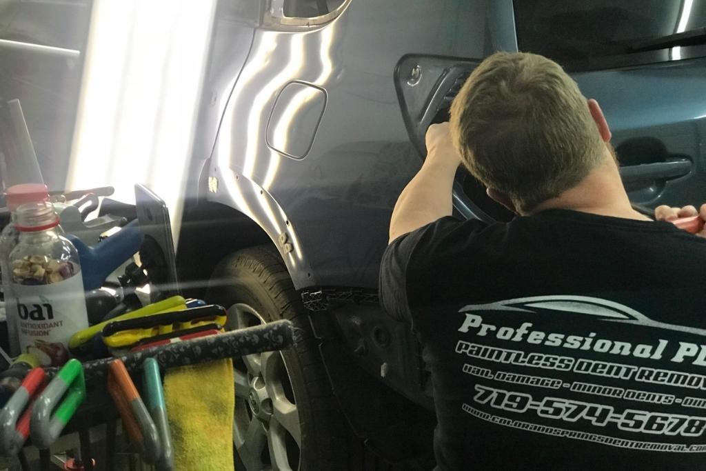 Auto technician from Professional PDR performing paintless dent repair on a dark-colored SUV, using specialized tools under bright lighting to restore the panel without repainting.