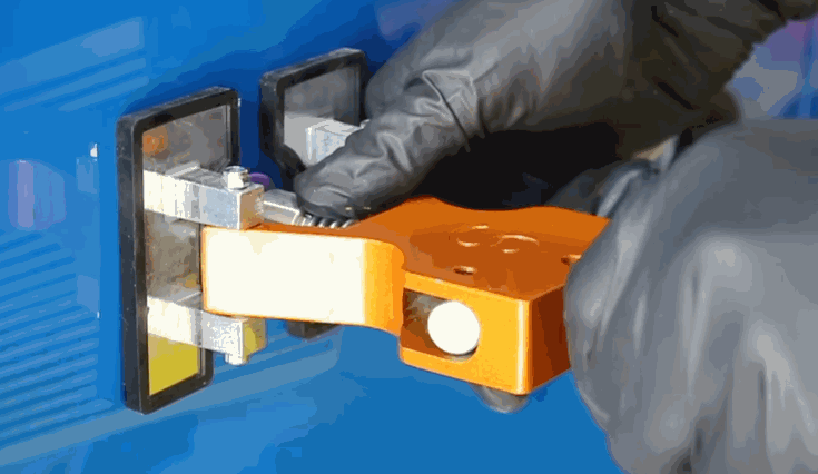 Close-up of a gloved technician using a dent repair pulling tool on a blue vehicle panel. The orange and silver device is securely attached to the surface to extract a dent.