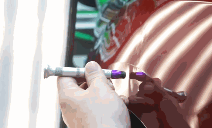 Close-up of a technician using a specialized tool to smooth out a dent on a red car fender during a fender bender repair.
