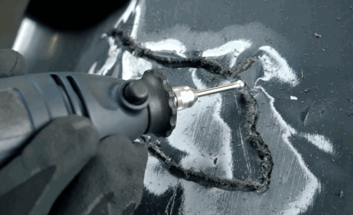 A rotary tool is used to smooth and clean the edges around a deep bumper crack during a detailed bumper repair process.