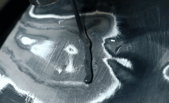 Close-up of a bumper with surface grinding marks and a long crack being prepared for bumper repair using a plastic welding tool.