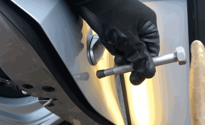 Close up of a gloved technician using a metal rod tool for Paintless Dent Repair on a car door panel with a reflection board to identify imperfections.