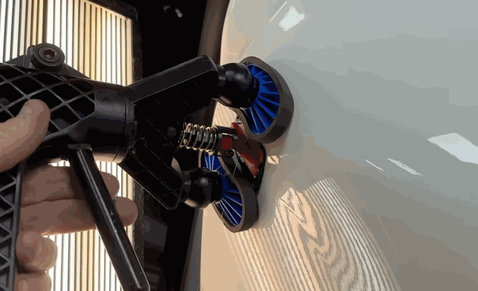 Close up of a glue pulling tool attached to a white vehicle panel during repair as striped reflection lighting reveals surface imperfections.