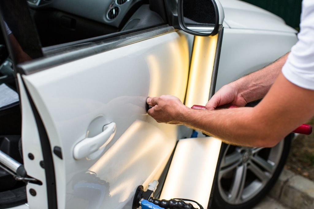 Technician performing paintless dent repair on a white car door using specialized dent removal tools