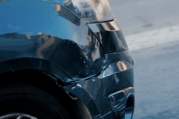 Close-up of a black car bumper and rear quarter panel with visible dents and scuff marks from a minor collision.