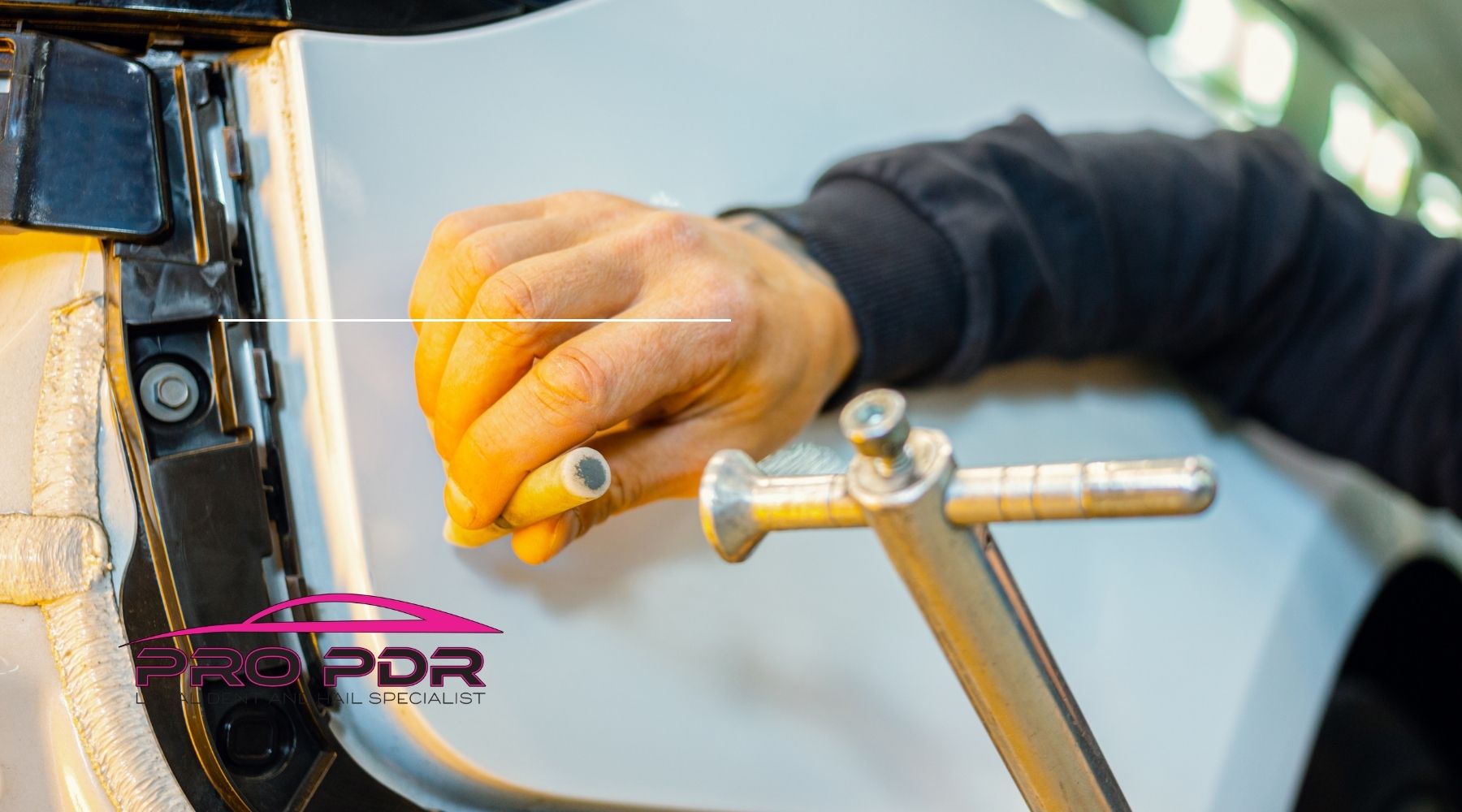 Technician performing paintless dent repair on a white car door using PDR tools