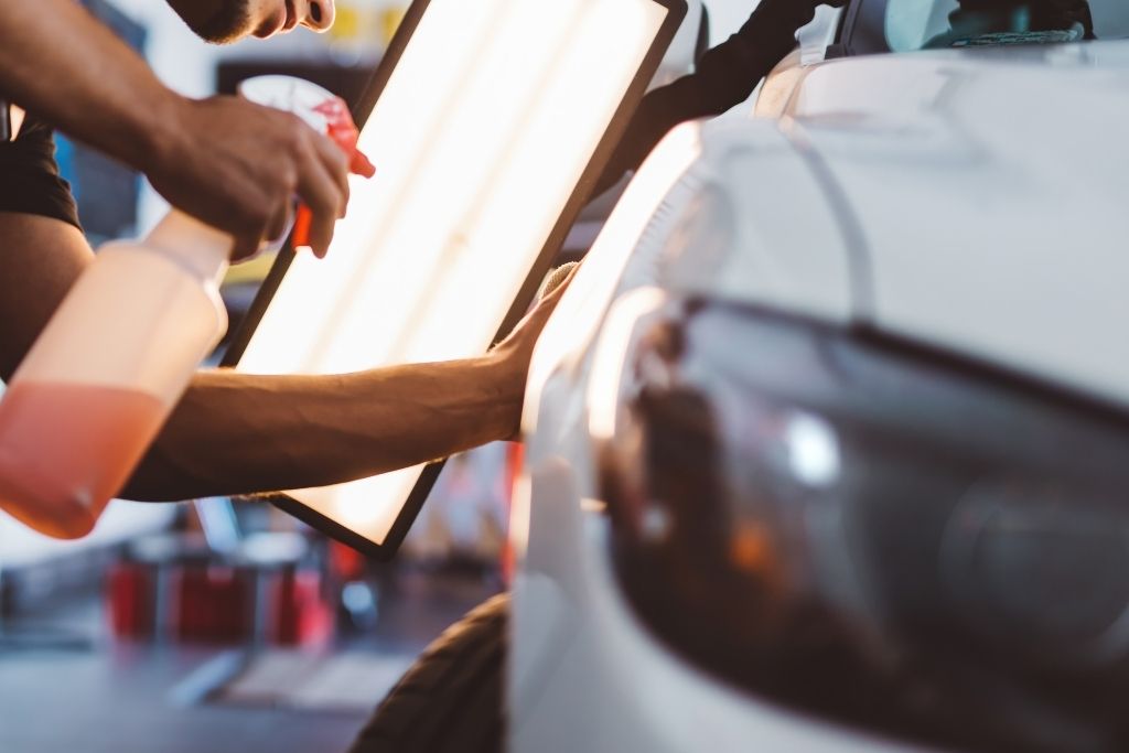 Technician inspecting a white vehicle with a PDR light during paintless dent repair