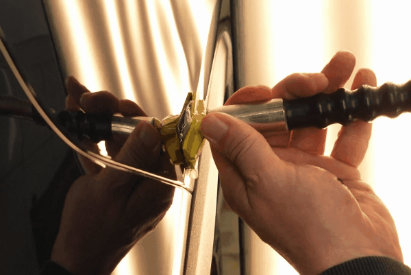 Close-up of paintless dent repair tool pulling a small dent from a vehicle panel