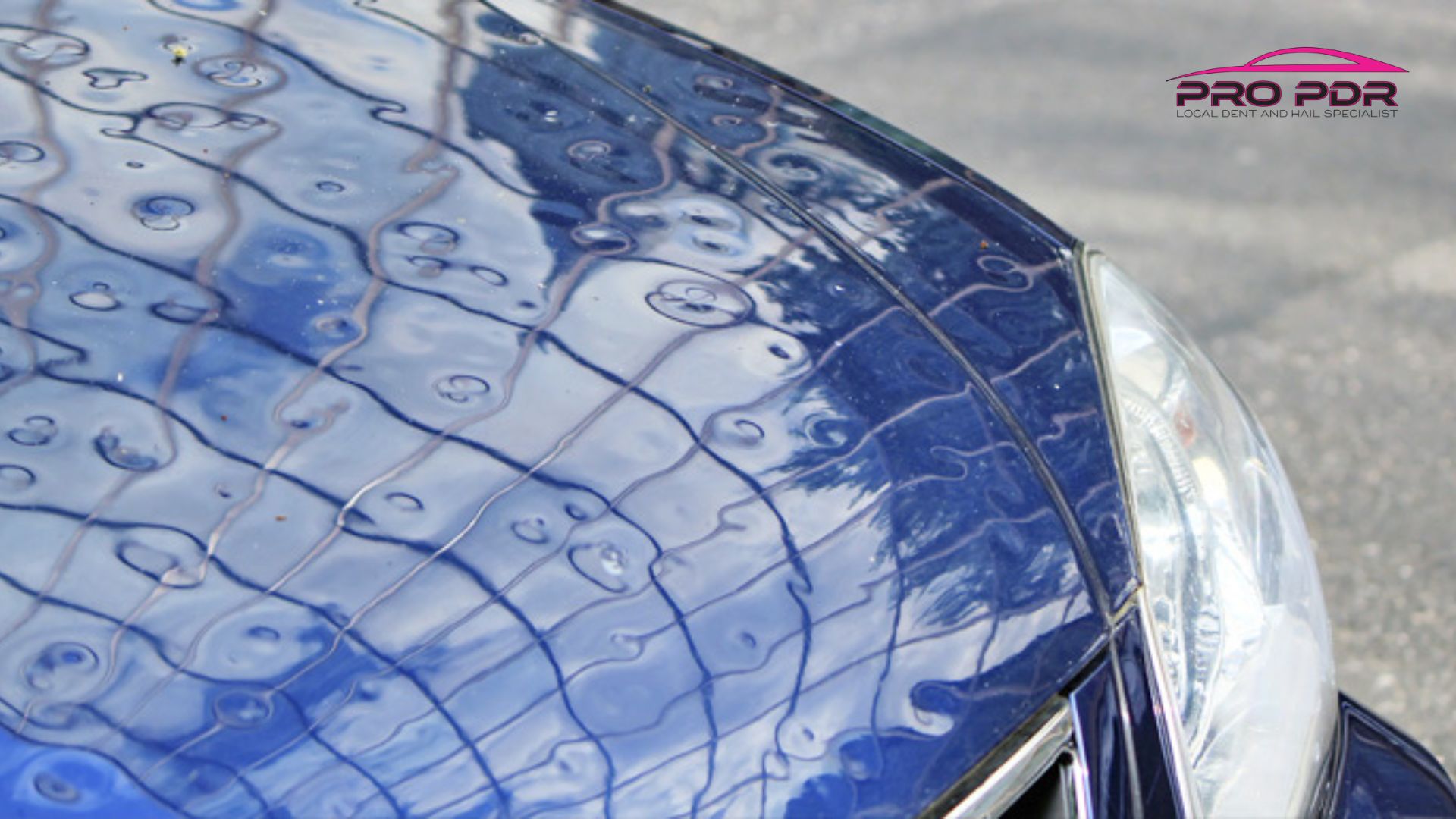 Close view of a blue car hood with visible dents and ripple patterns from hail damage, highlighted by reflections and grid lines across the surface.