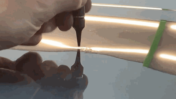 A hand uses a fine repair tool on a small dent in a car panel during hail damage repair.