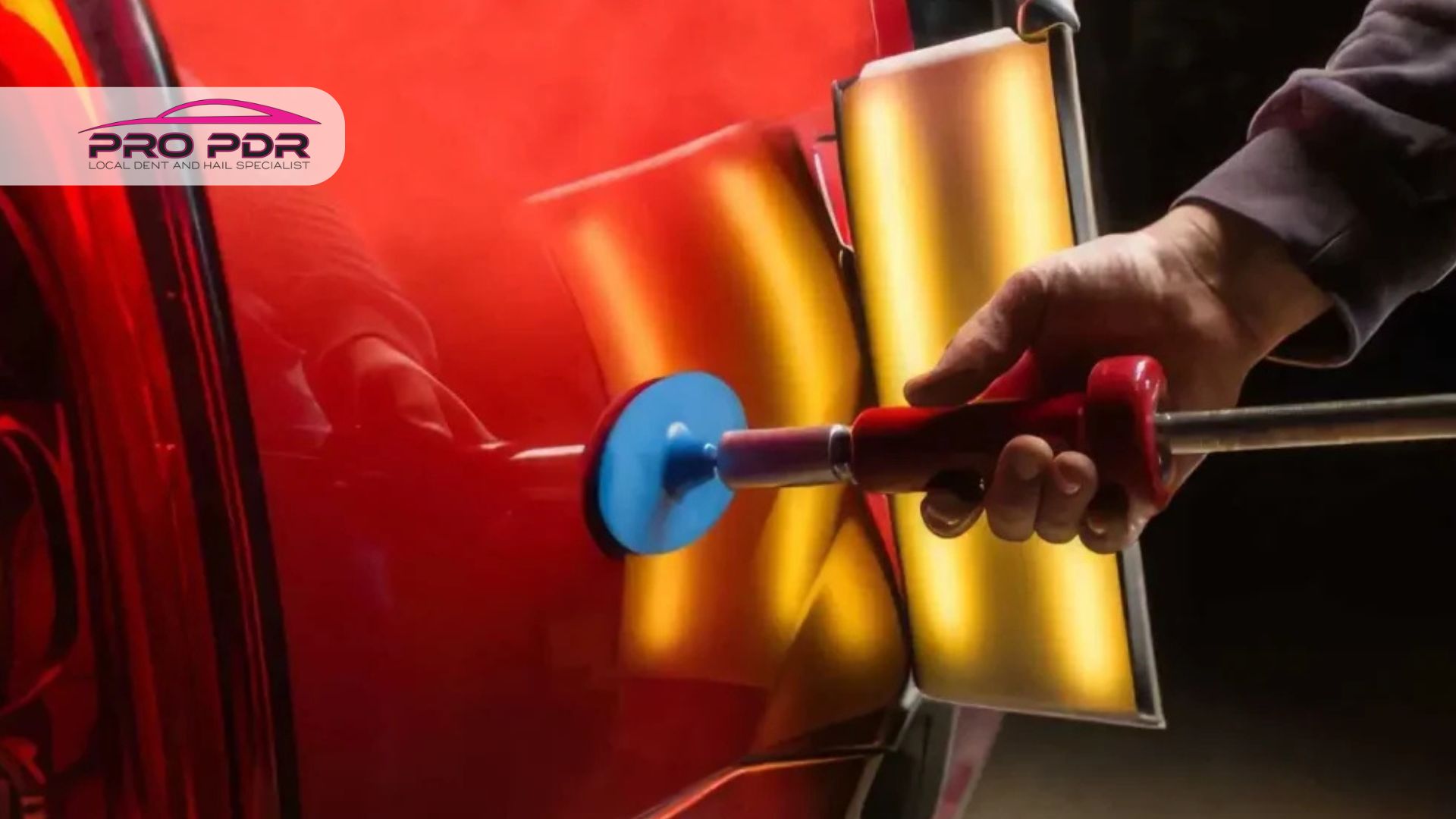 Paintless dent repair technician removing hail damage from a red vehicle using professional dent repair tools.