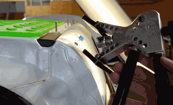 A close up shows a hail damage repair tool positioned against a dented silver vehicle panel under a reflection light. A green tab board sits on the panel to help guide the repair process.
