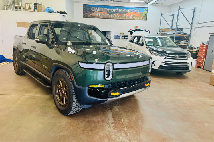 Green electric truck in a garage, showcasing paint protection film and ceramic coating, with a white SUV in the background, emphasizing surface protection services by Pro PDR.