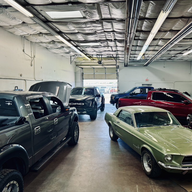 Cars in a repair shop, featuring a vintage green Mustang, a gray pickup truck, and a black Ford truck, showcasing Pro PDR's paintless dent repair services.